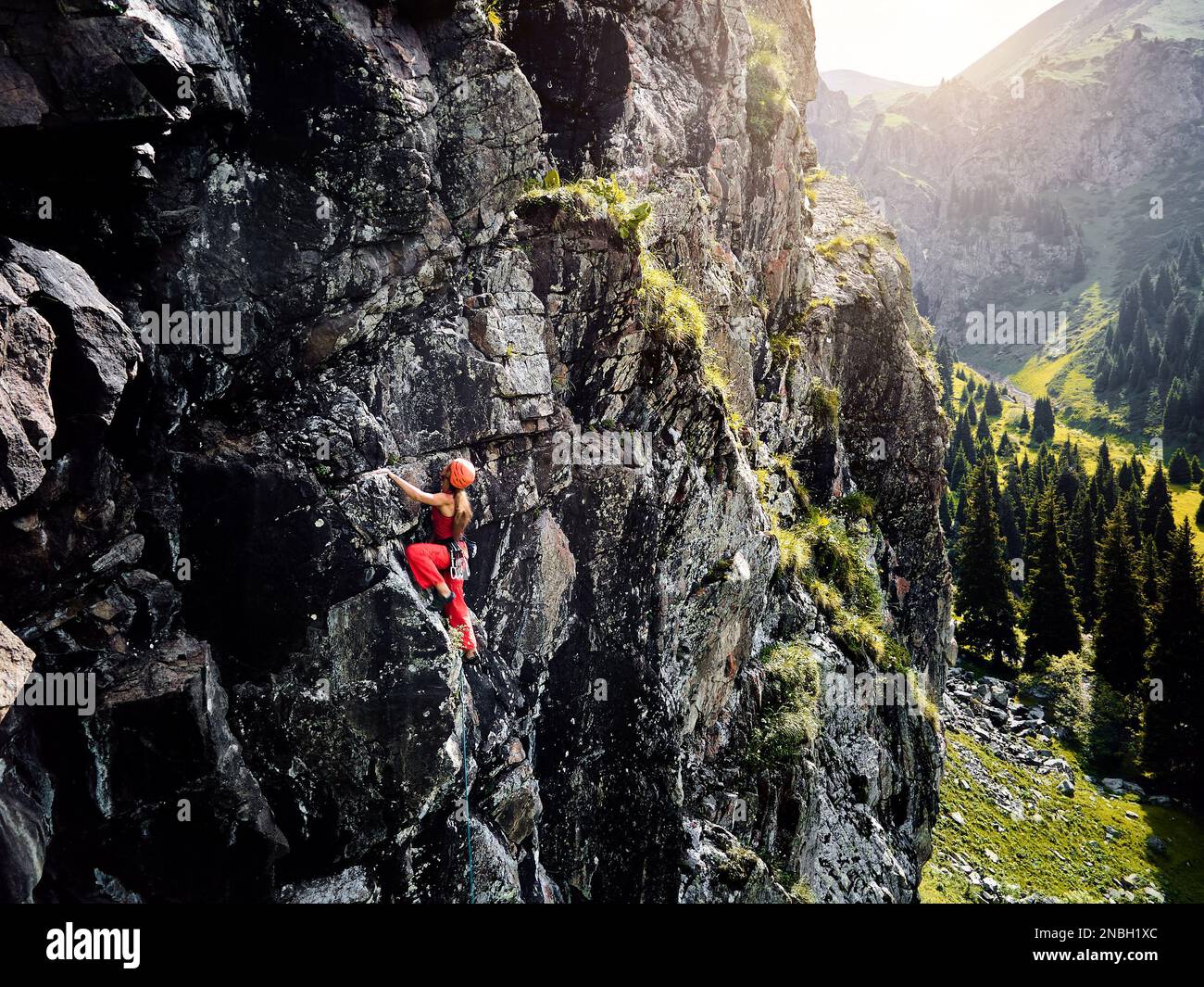 Drohnenaufnahme einer starken Frau im roten Hemd, die auf dem hohen Felsen in den Bergen Tyan Shan in Kasachstan klettert Stockfoto