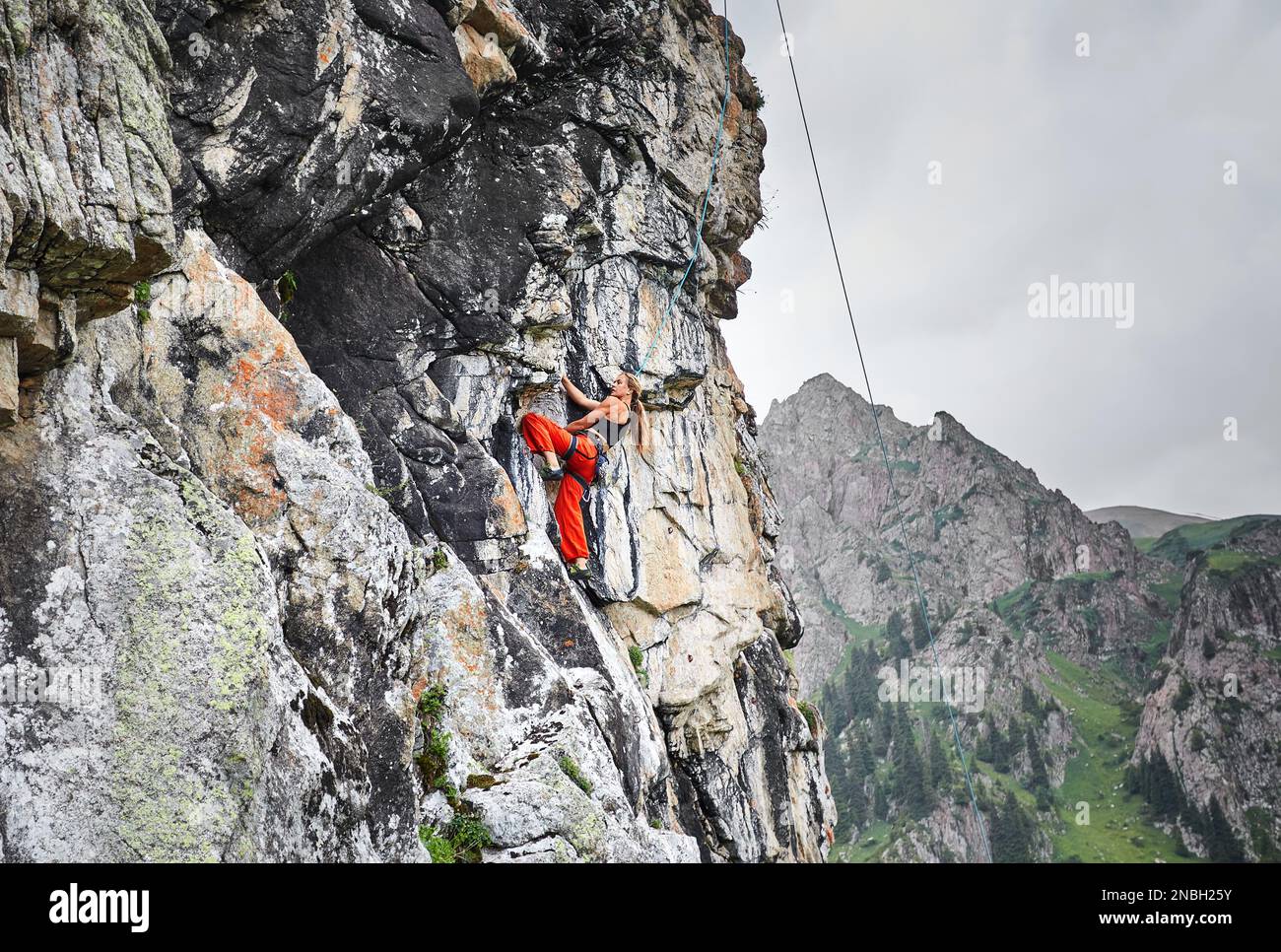 Portrait of Fit starke Frau in roten Hosen klettert auf den hohen vertikalen Felsen in den Bergen Tyan Shan in Kasachstan Stockfoto