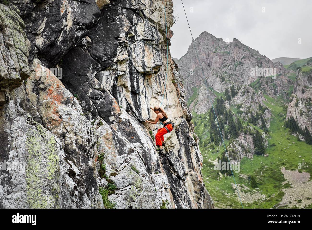 Portrait of Fit starke Frau in roten Hosen klettert auf den hohen vertikalen Felsen in den Bergen Tyan Shan in Kasachstan Stockfoto