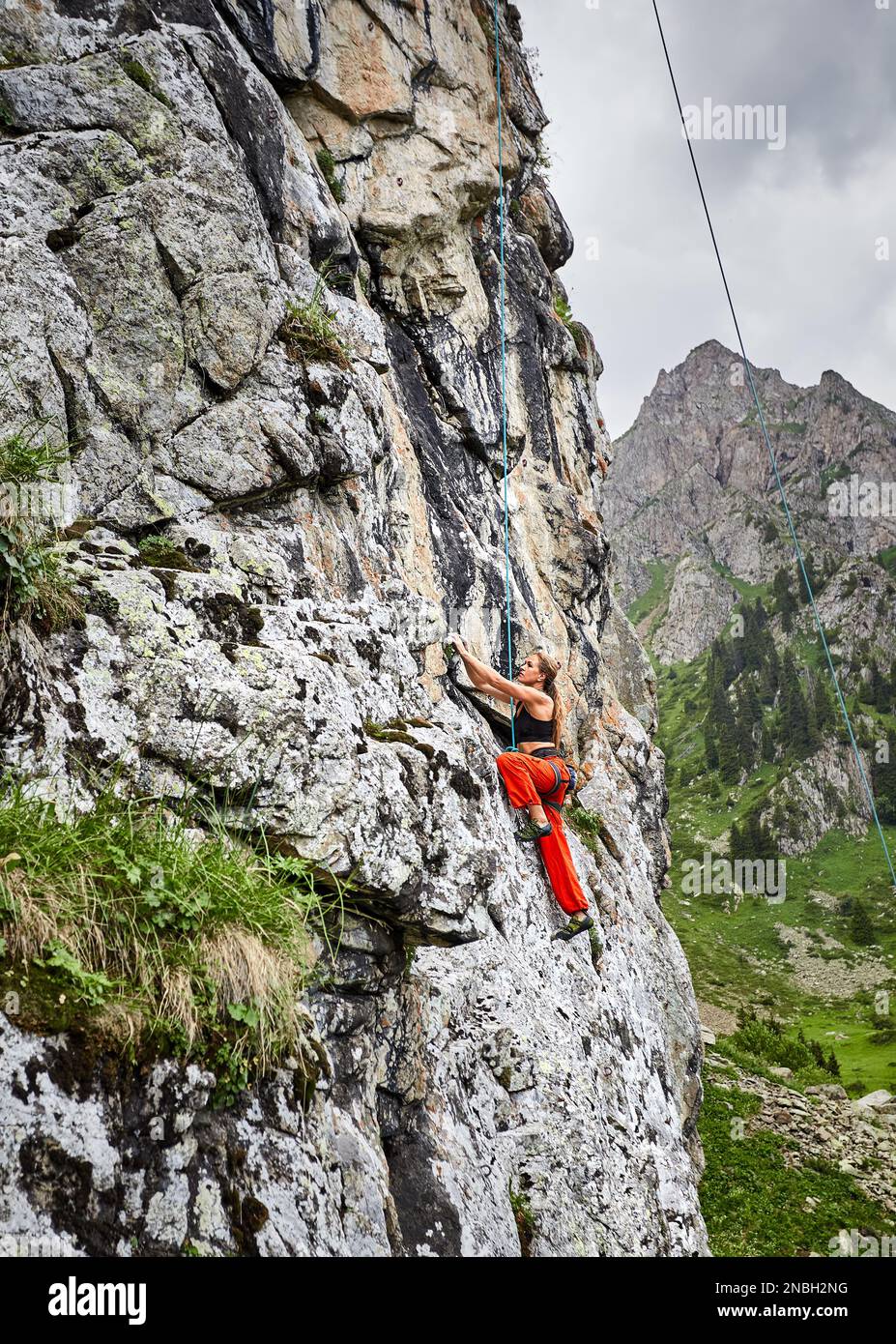 Portrait of Fit starke Frau in roten Hosen klettert auf den hohen vertikalen Felsen in den Bergen Tyan Shan in Kasachstan Stockfoto