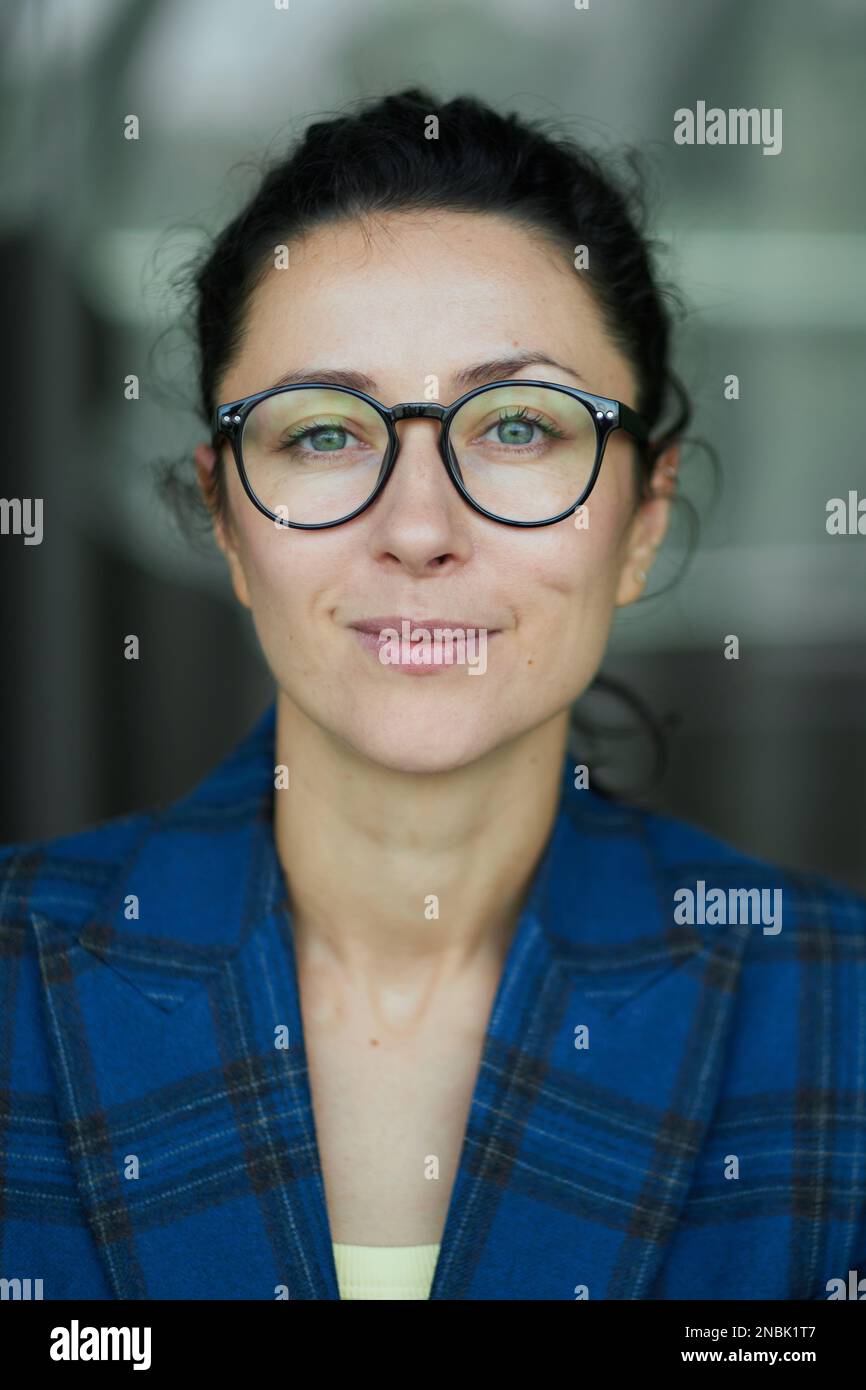 Porträt einer Geschäftsfrau mit einer lächelnden Brille. Dunkelblaue Jacke, selbstbewusste Frau, die in die Kamera schaut Hochwertiges Foto Stockfoto