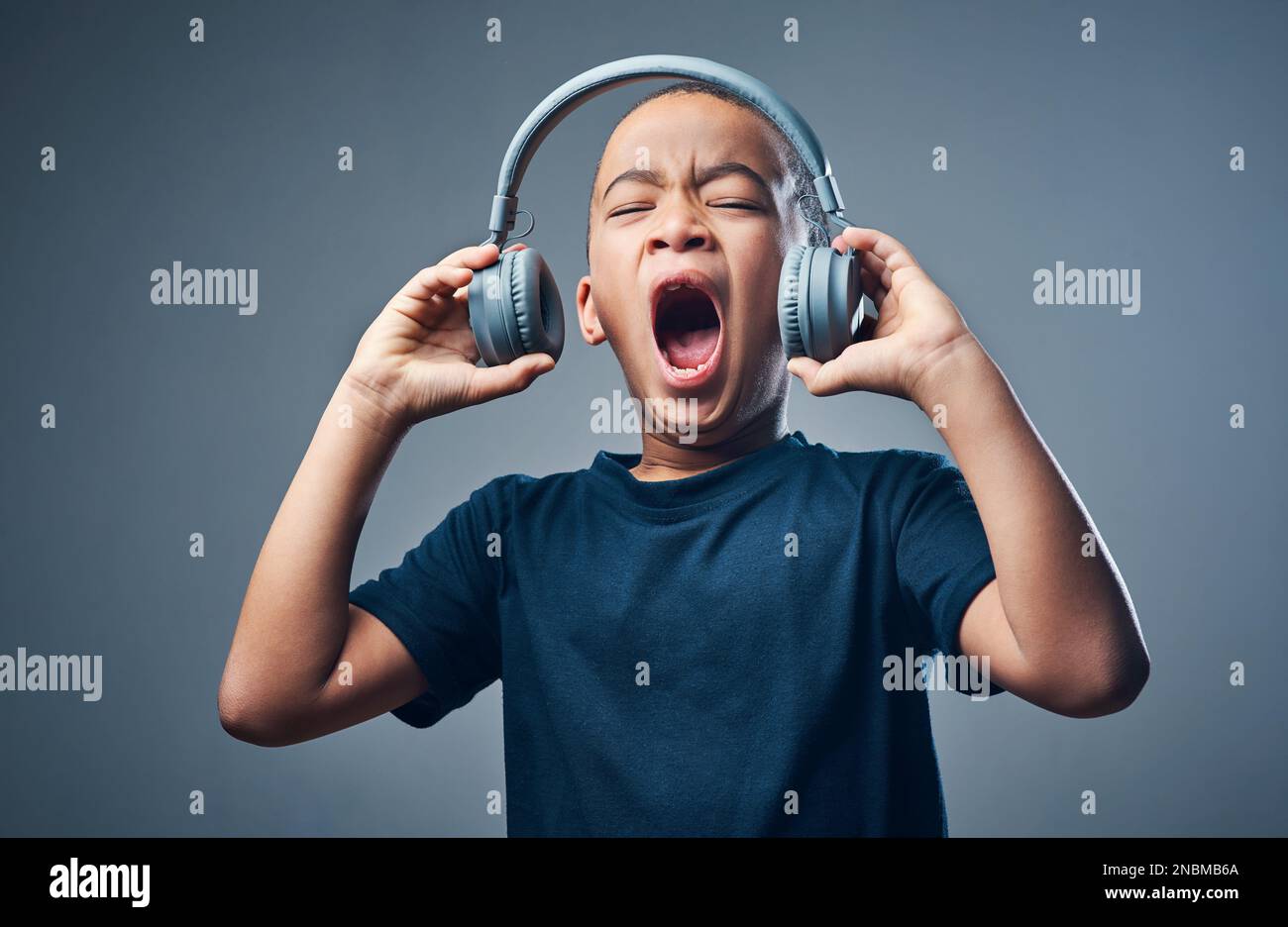 Mit kräftigen Bässen macht es viel Spaß. Studioaufnahme eines süßen kleinen Jungen, der Kopfhörer mit offenem Mund vor grauem Hintergrund verwendet. Stockfoto