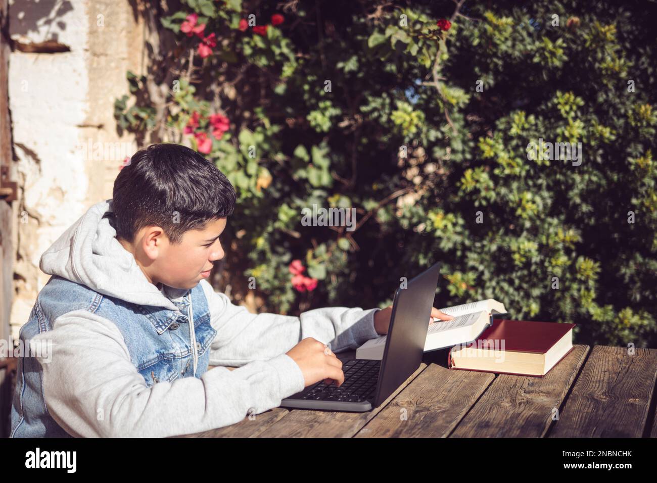 Ein junger latino liest draußen vor dem Laptop ein Buch Stockfoto