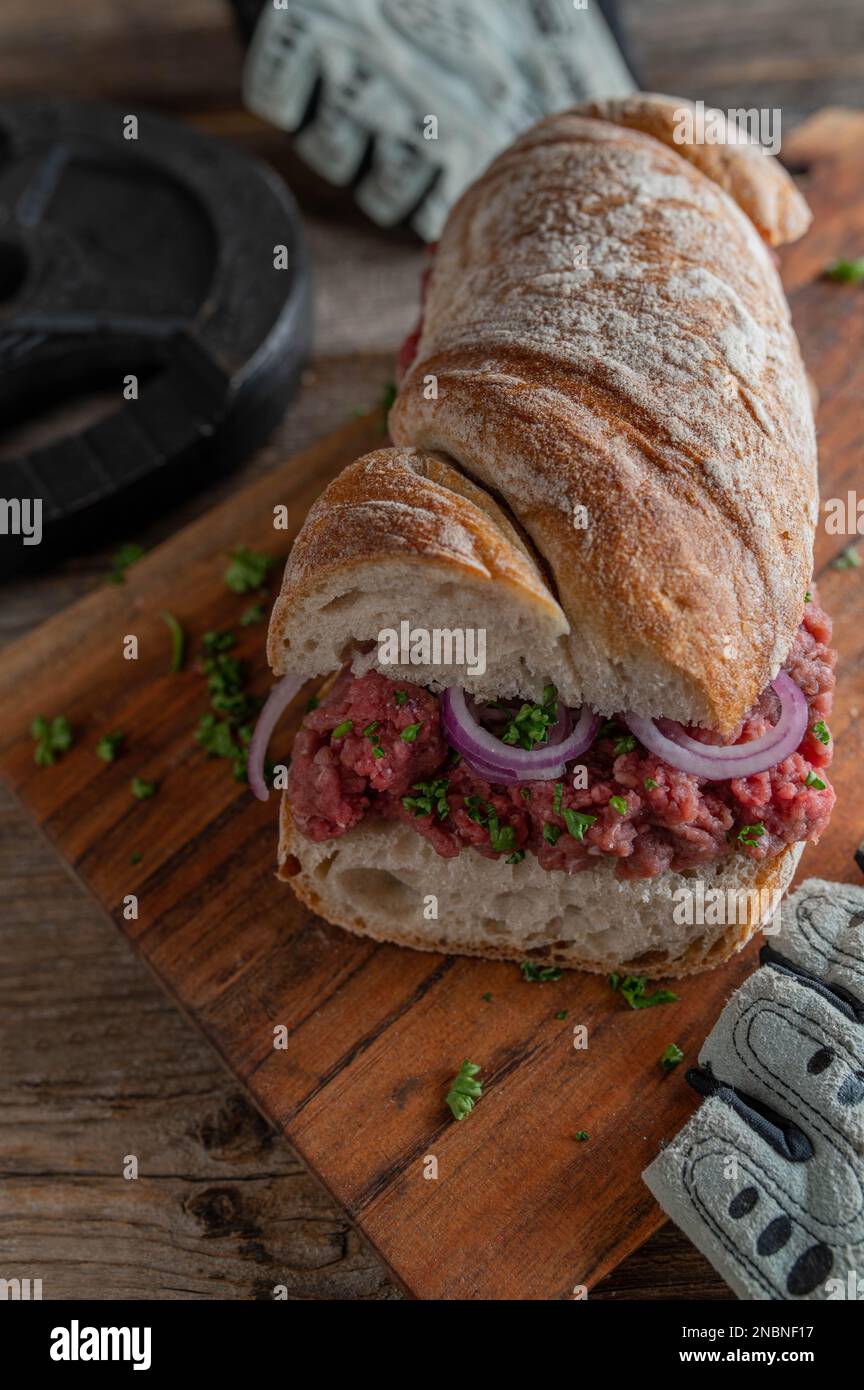Rohes Rindfleisch-Sandwich auf rustikalem Baguette-Brot mit roten Zwiebeln und Petersilie auf einem Holztisch Stockfoto