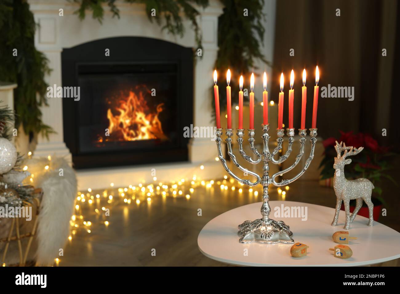 Silberne Menora in der Nähe von Dreidel mit den Symbolen Nun, Gimel, He, PE im Zimmer gegen Kamin, Platz für Text Stockfoto