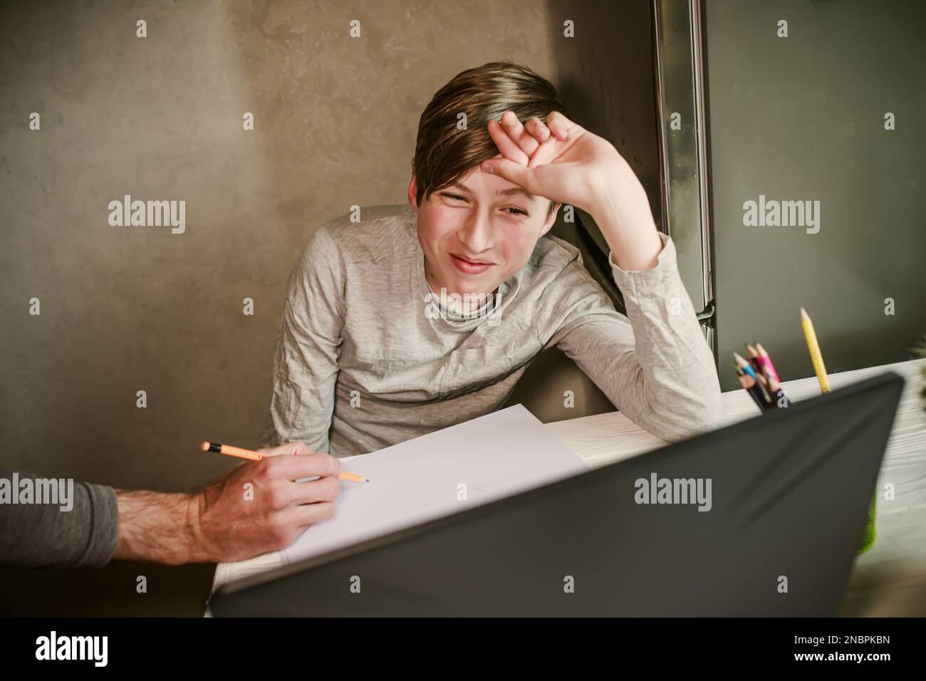 Der Junge schaut zu seinem Vater auf, der ihm bei den Hausaufgaben hilft. Der Schüler beantwortet die Frage des Lehrers, während er online auf einem Laptop lernt. Kinderhand Stockfoto