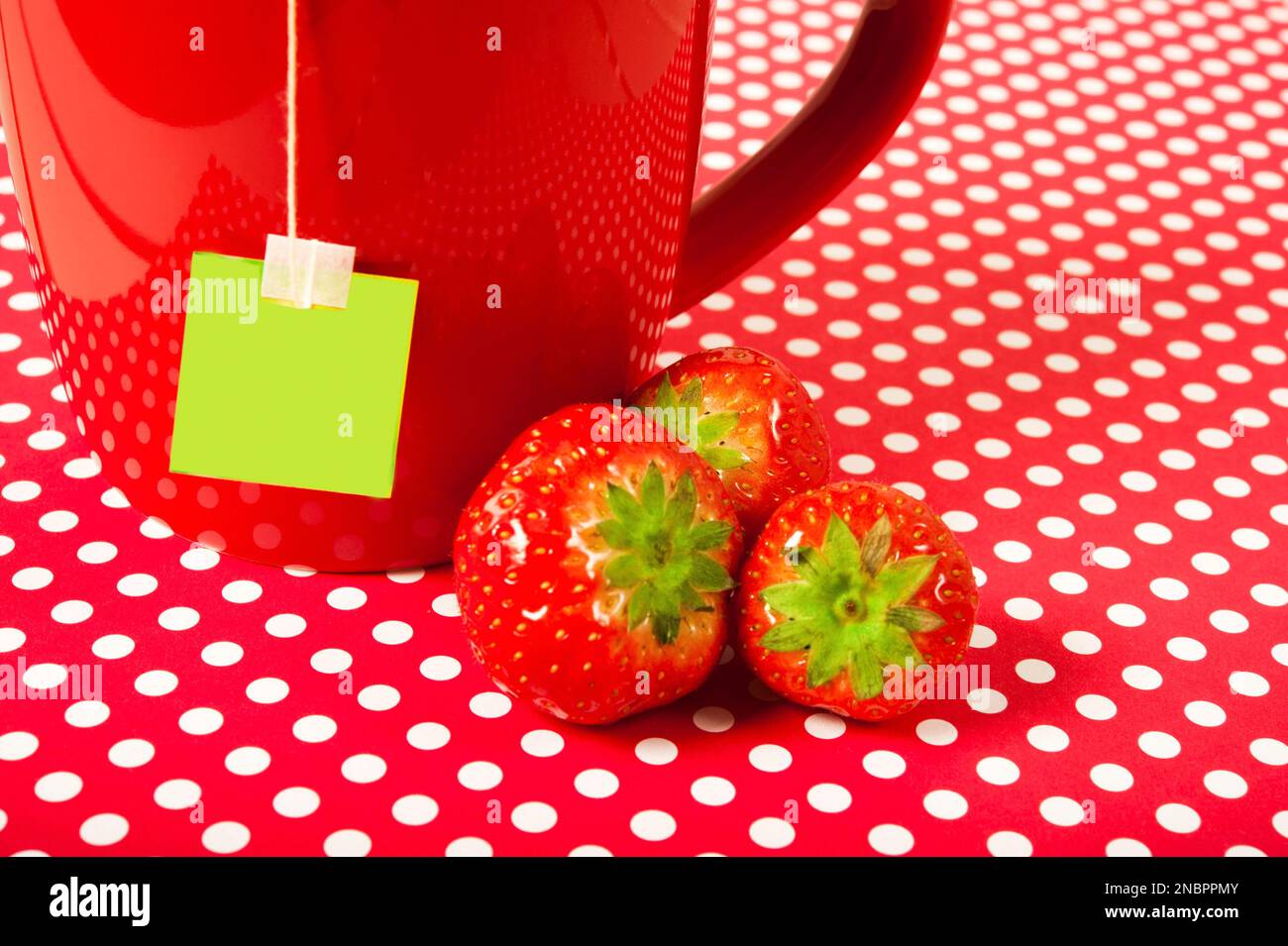 Roter Becher mit Teebeutel und Erdbeeren auf rot-weißen Polka-Punkten Hintergrund wie fröhliches Konzept von Obsttee Stockfoto