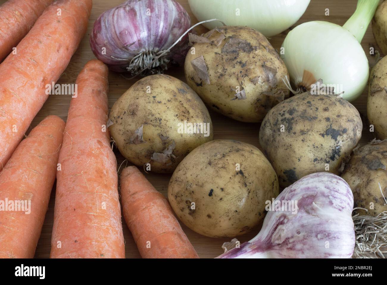 Bei der Herbsternte ergänzen Kartoffeln, die auf einem Holztisch neben Möhren, Knoblauch und Zwiebeln liegen, die Zusammensetzung des Gemüses und des Kochens Stockfoto