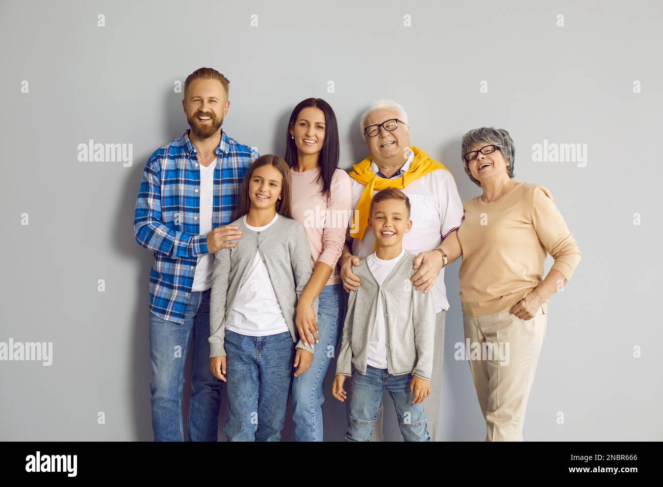 Gruppenporträt einer glücklichen Familie, die alle zusammen an einer grauen Wand im Studio steht Stockfoto