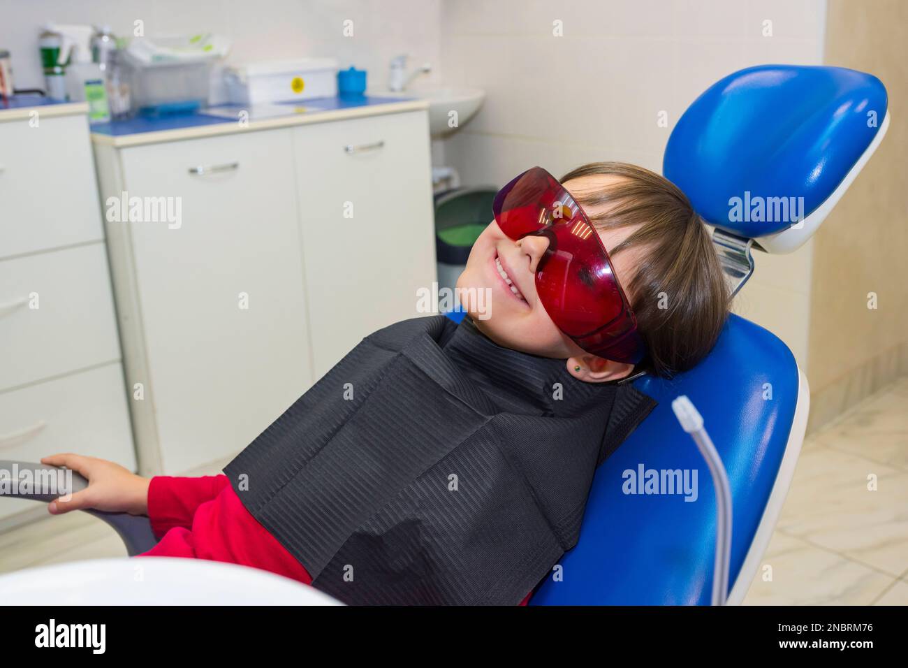 Glücklicher Kindspatient mit Schutzbrille, sitzt auf dem zahnärztlichen Stuhl Stockfoto