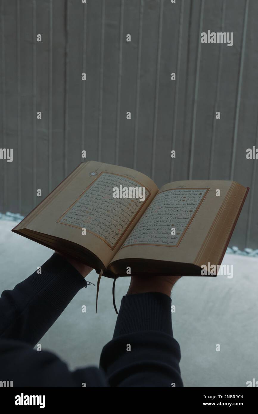 Der heilige Koran an den Händen eines muslimischen Mannes. Muslimischer Mann, der Koran in der Moschee liest. Islamisches vertikales Hintergrundbild. Istanbul Turkiye - 11.12.2022 Stockfoto
