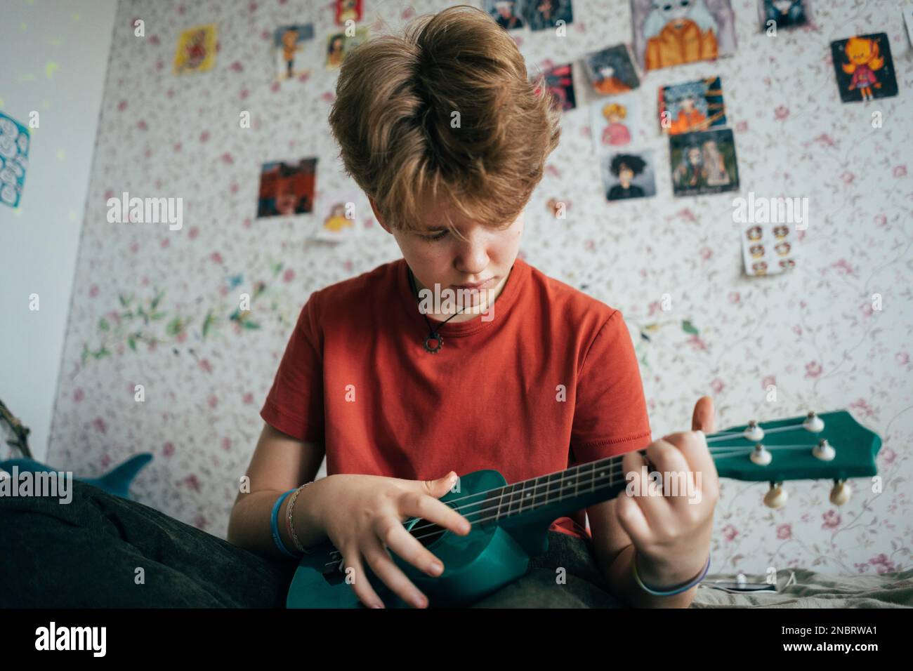 Ein Mädchen im Teenageralter, das auf dem Bett sitzt, lernt Ukulele zu spielen. Stockfoto