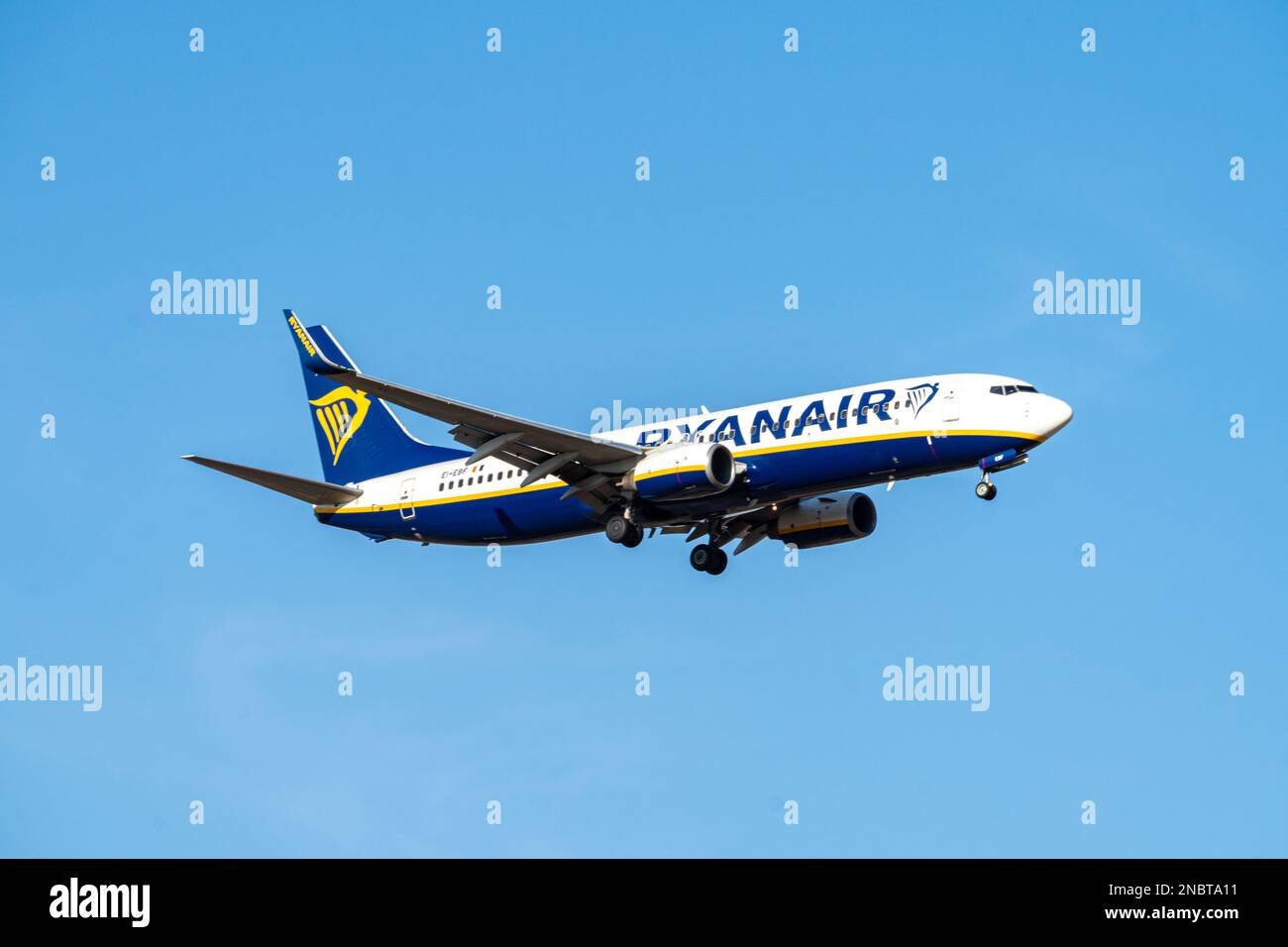 Weißes, blaues und gelbes Flugzeug der Ryanair-Fluggesellschaft mit irischer Flagge und Ei-EF-Registrierung, wobei sich das Fahrwerk unten nähert und in Madrid Barajas landet. Stockfoto