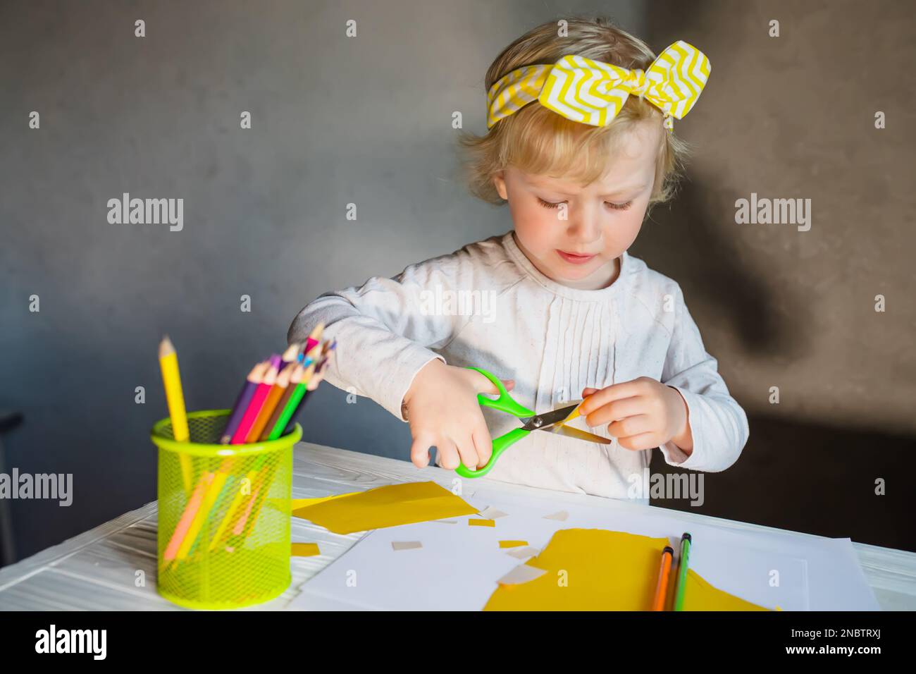 Kreativität mit Kindern. Funktioniert aus Papier. Das Baby schneidet Details für die Muttertagskarte mit einer grünen Schere aus Papier aus Stockfoto