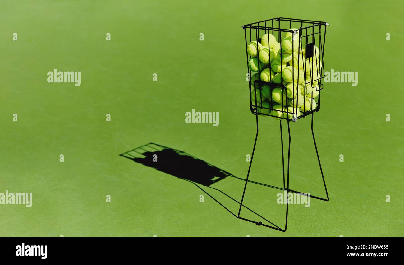 Tennis, Sportballkorb, Sportplatz auf einem grünen Trainingsplatz draußen ohne Leute. Sport-, Fitness- und Trainingsgeräte im Schatten für das Spiel Stockfoto