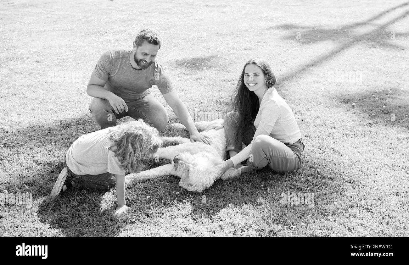 Glückliche Familie von Mutter Vater und Kind Sohn spielen mit Hund im Sommer Park grünen Gras, Adoption Stockfoto