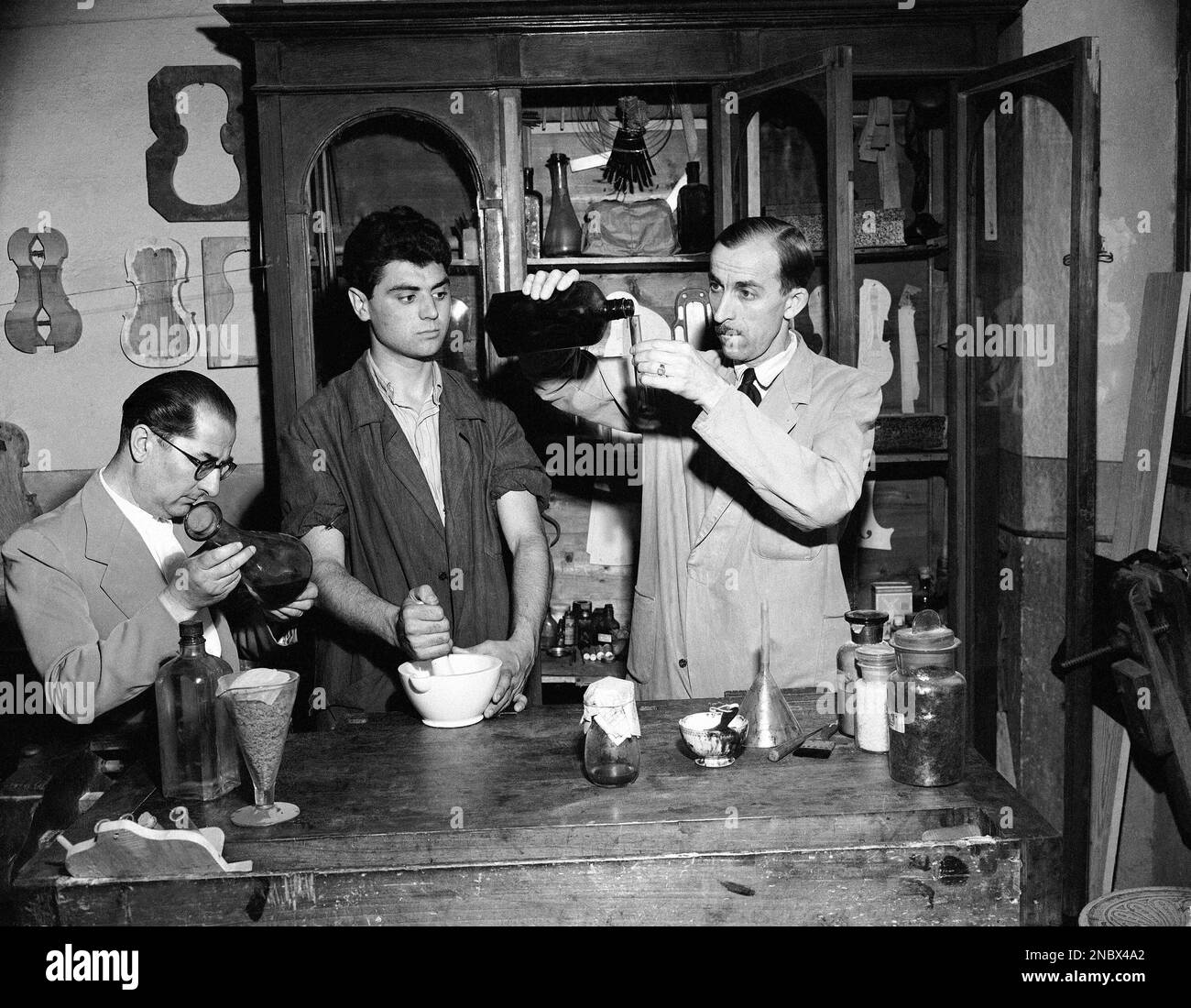 At the International School of Violin Making in Cremona, Italy on June 23, 1949, they are mixing chemicals for varnish for violins. One of the great secrets of Antonio Stradivari, master violin maker of the late 17th and early 18th centuries, whose hometown was Cremona, was his varnish. It was soft in texture and shaded from orange to red. Left to right: Professor Renzo Bacchetta, lawyer, who runs the school; student Ercole Ghisolfi; and Peter Tater, principal and teacher at the school. (AP Photo/Jim Pringle) Stockfoto