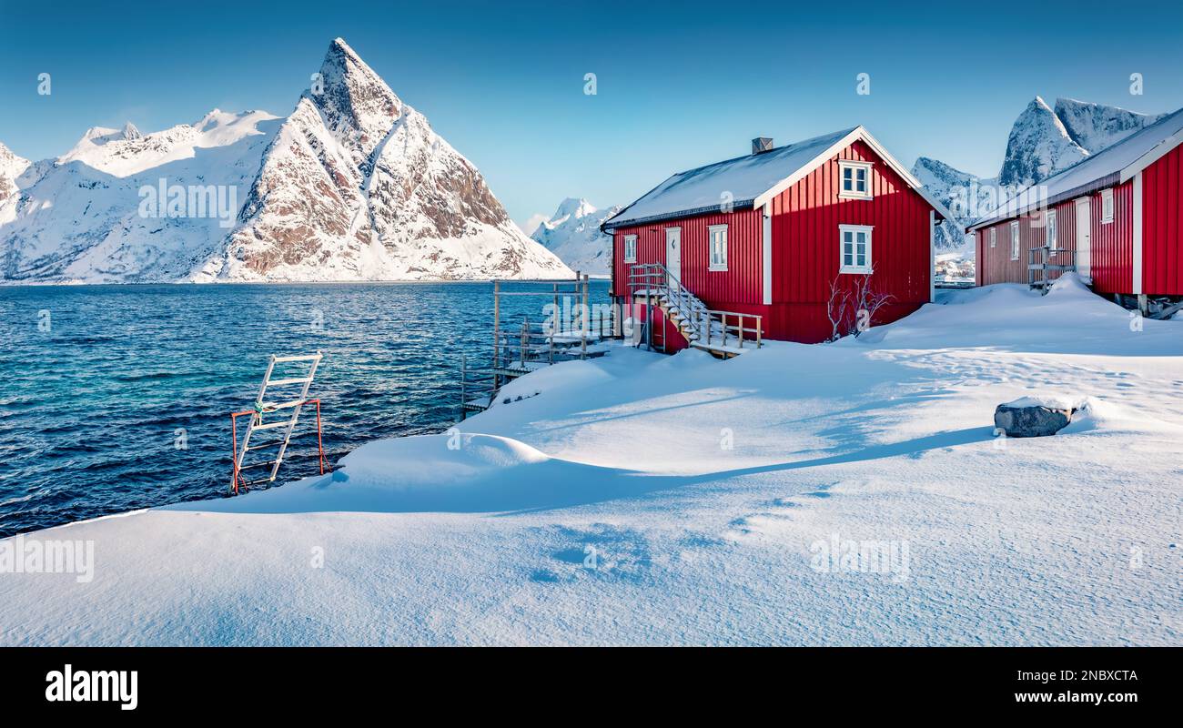 Weihnachtspostkarte. Rote Holzhäuser am Ufer des norwegischen Meeres. Malerischer Winterblick auf das Dorf Hamnoy und die Lofoten-Inseln. Frostige Morgenszene Stockfoto