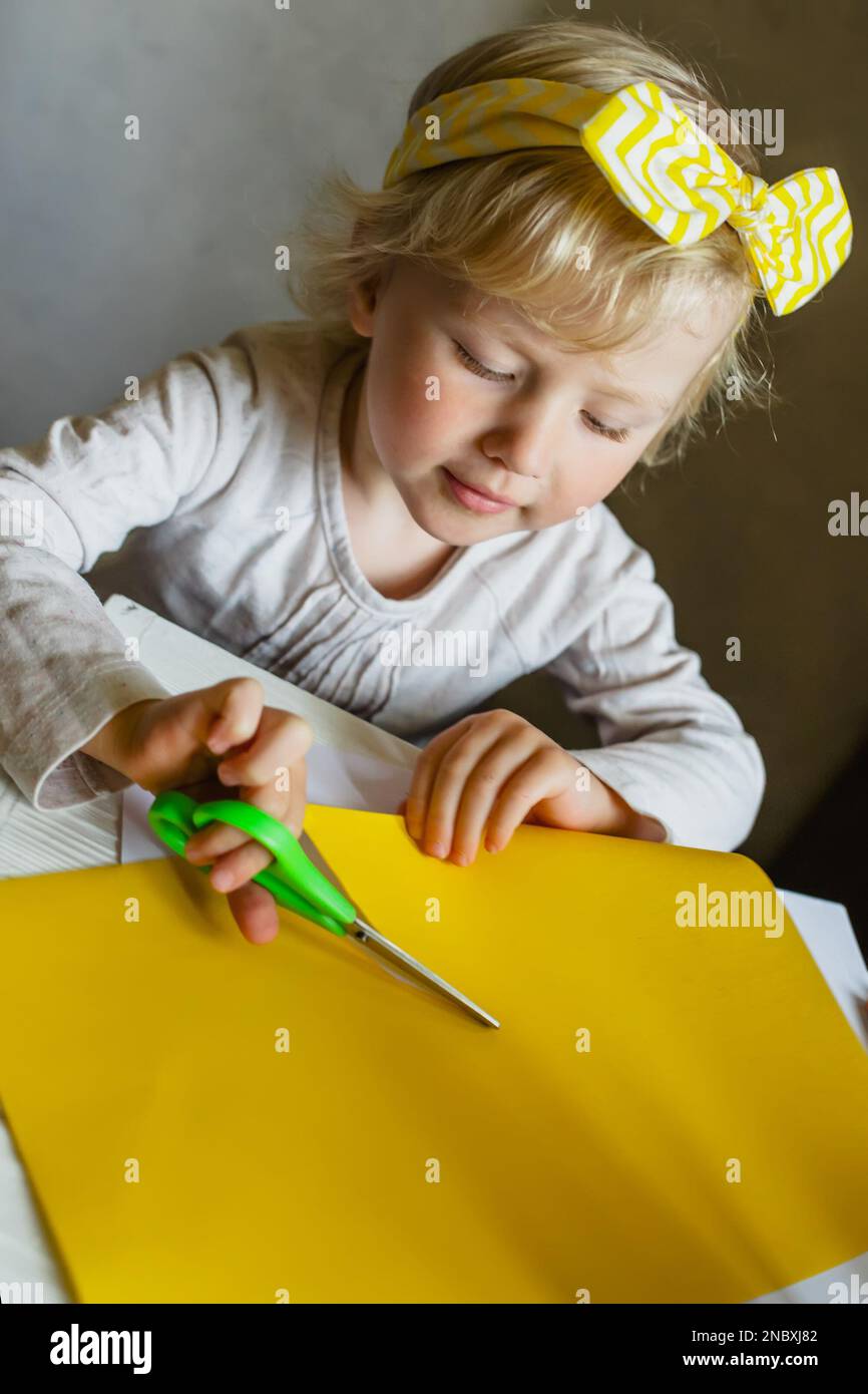 Vorschulkindern Scheren-Fähigkeiten beibringen. Farbiges gelbes Papier mit Schere am Tisch Stockfoto