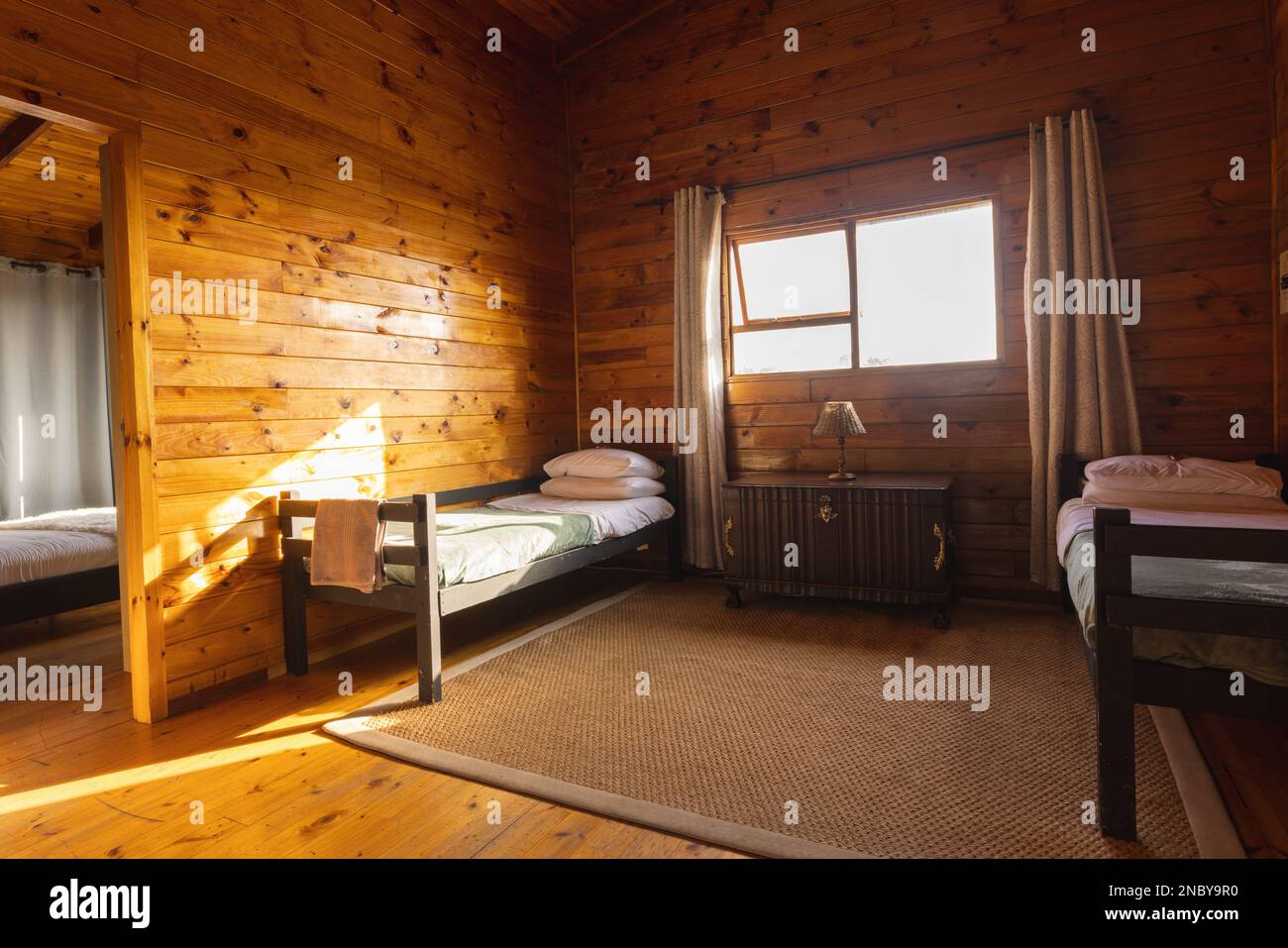 Leeres, gemütliches Zimmer in einer Blockhütte mit zwei Betten und einem großen Teppich. Holzkabine und Lifestyle-Konzept. Stockfoto