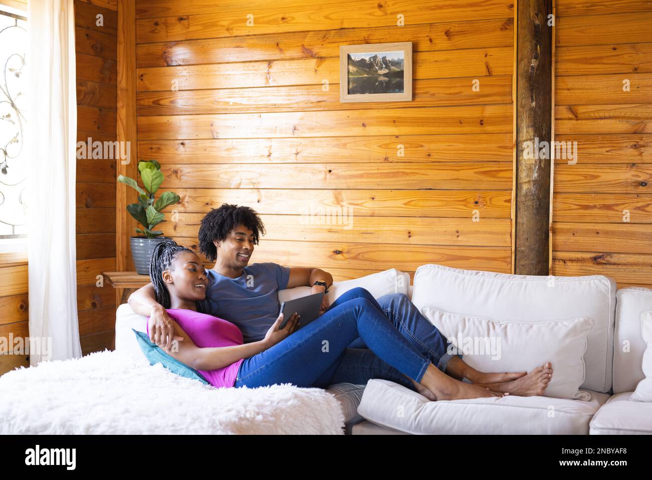 Glückliches afroamerikanisches Paar, das Zeit in einer Blockhütte mit einem Tablet verbringt. Blockhütte, Natur- und Lifestyle-Konzept. Stockfoto