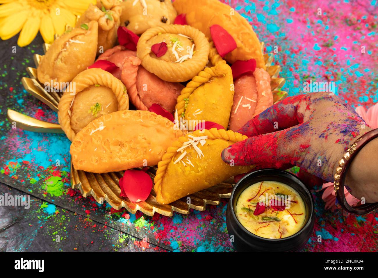 Hände eines Mädchens gemalt mit farbenfrohem Gulal Holding köstliches Gujiya auch genannt Gujia, Ghughra, Karanji, Somas, Garijalu, Kajikayalu, Karigadubu, Gu Stockfoto