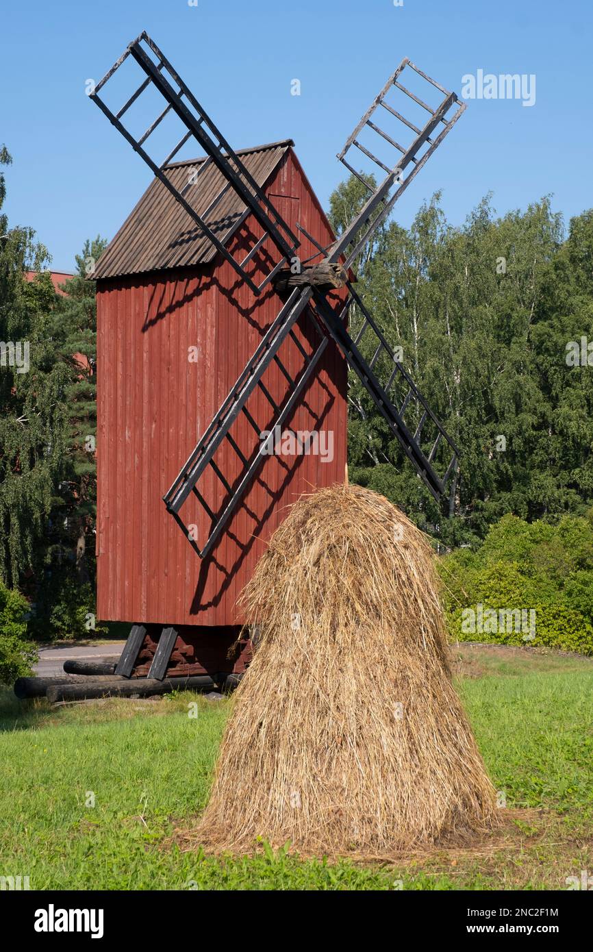 Helsinki / Finnland - 14. AUGUST 2022 - alte rote Holzwindmühle mit einem Heuhaufen im Vordergrund. Finnische Landwirtschaft. Stockfoto
