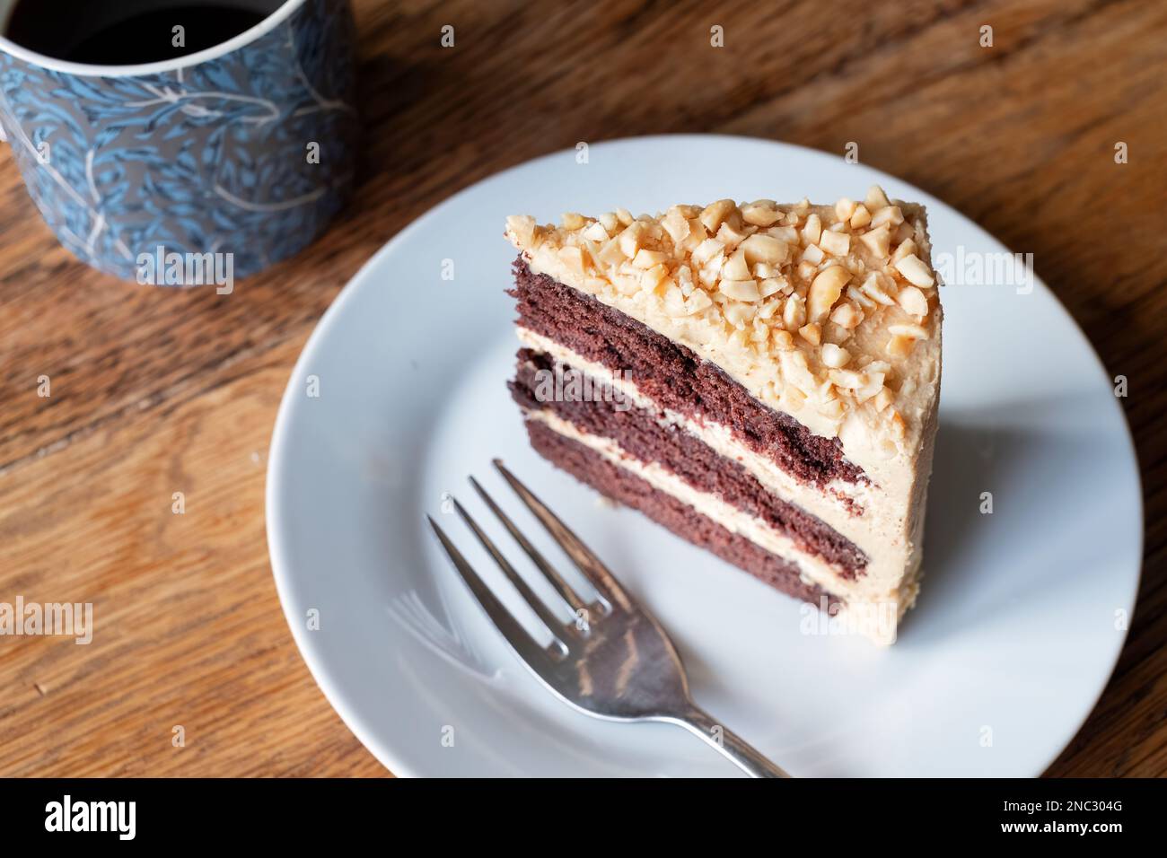 Ein Stück frisch gebackene Erdnussbutter und Schokoladenkuchen. Der Kuchen ist mit einer dicken Buttercreme gefüllt und wird zusammen mit einer Tasse Tee auf einem Beilagenteller serviert Stockfoto