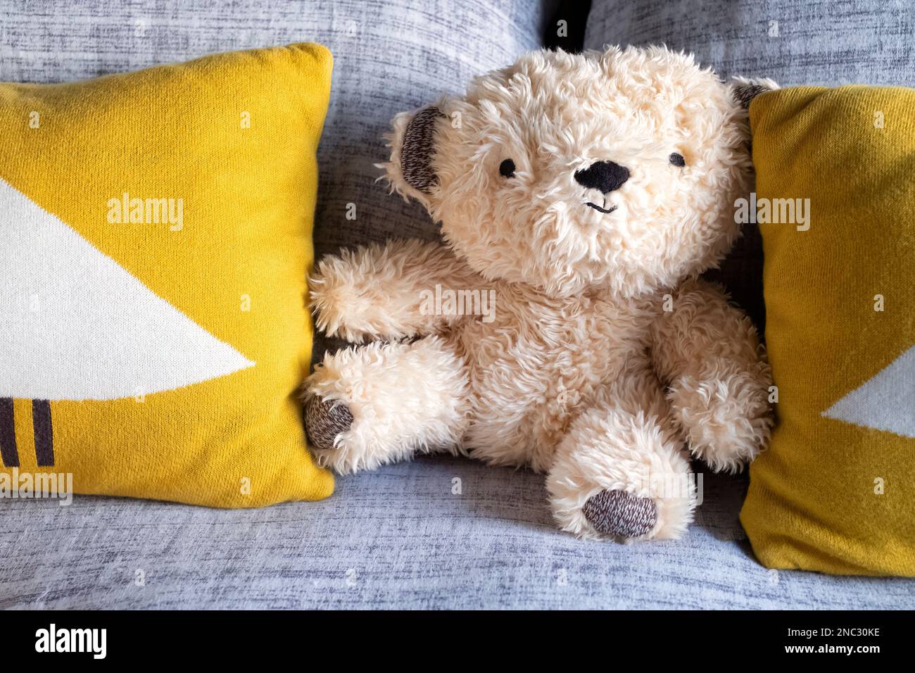 Ein kleiner, kuscheliger, pelziger Teddybär mit einem freundlichen Gesicht, auf einem Bett zwischen zwei Kissen platziert. Der Teddy gibt dem Schlafzimmer ein schönes persönliches Zuhause Stockfoto