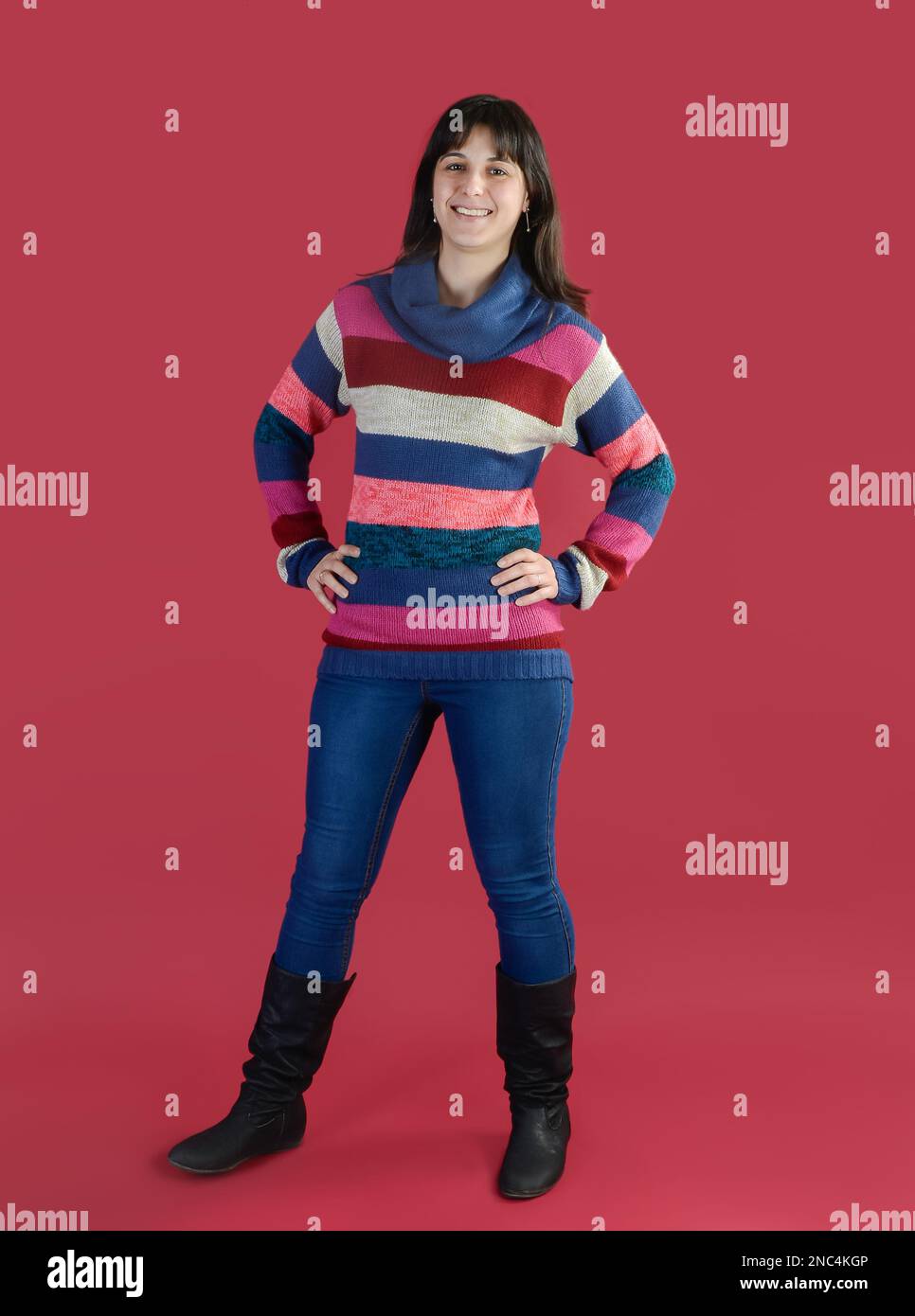 Eine junge Frau lächelt in einem gestreiften Pullover auf den Füßen auf einem magentafarbenen Hintergrund. Stockfoto