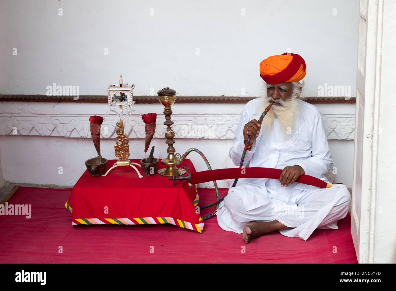 Jodhpur, Rajasthan, Indien - 19. Oktober 2019: Rajput Senior man raucht durch eine Wasserpfeife, trägt Marathi Pagri und Schwert auf den Knien. Stockfoto