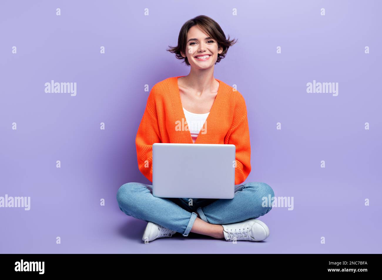 Foto in voller Länge von einer jungen, fröhlichen Designerfrau, die sitzt, verwenden einen persönlichen Laptop und genießen ihren Job isoliert auf violettem Hintergrund Stockfoto