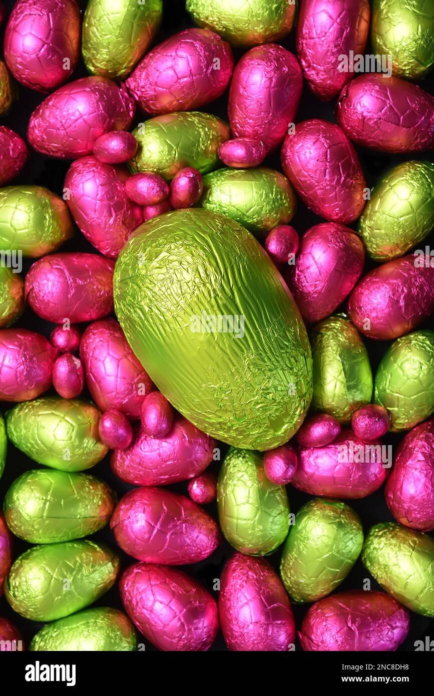 Ein Stapel mehrfarbiger und in verschiedenen Größen gebündelter Schokoladeneier in Pink und Grün, mit einem großen limiengrünen Ei. Stockfoto