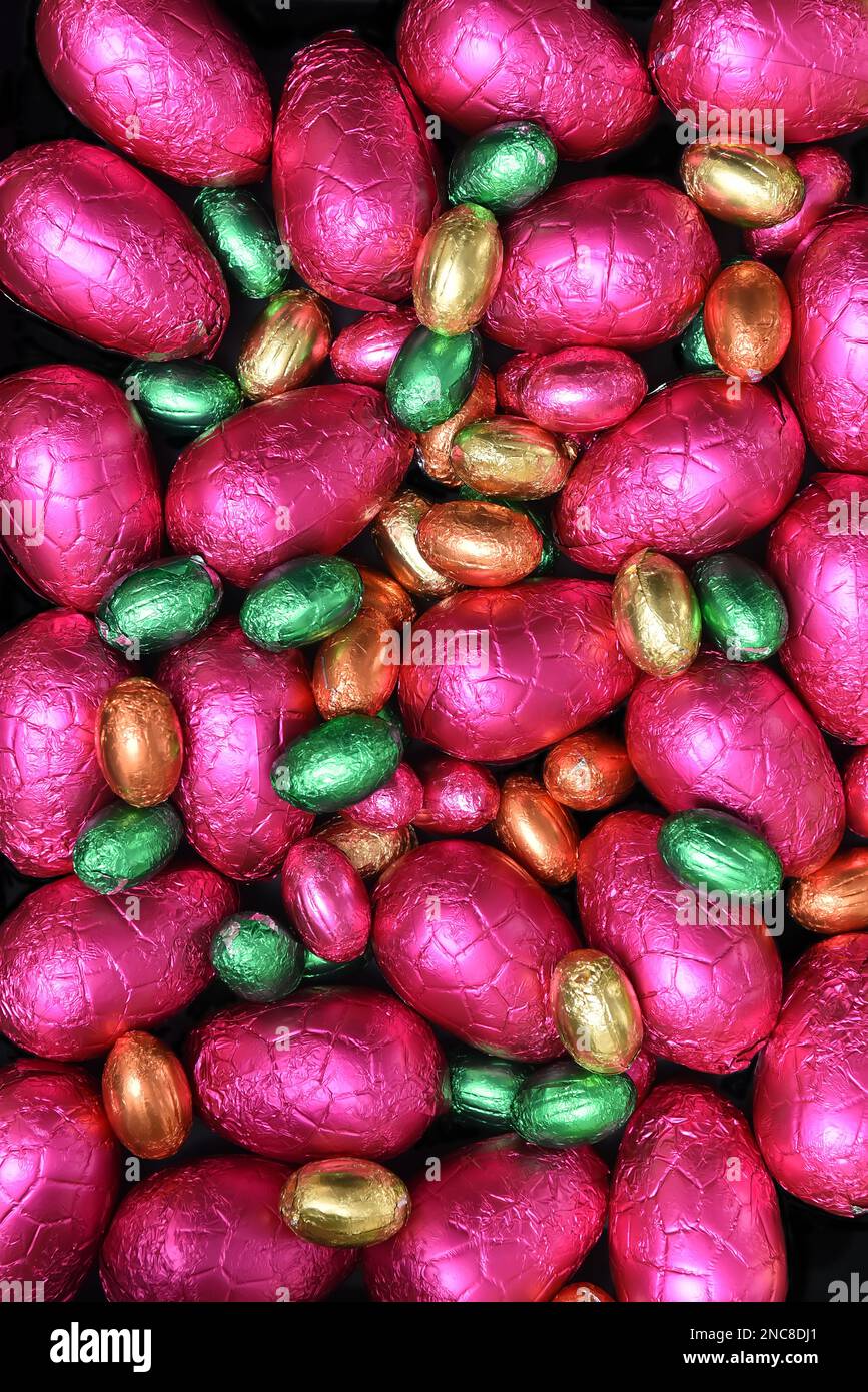 Stapel oder Gruppe von bunten, in Folie verpackten Schokoladeneiern in verschiedenen Größen in Pink, Rot, Gold, Orange und Limettengrün. Stockfoto