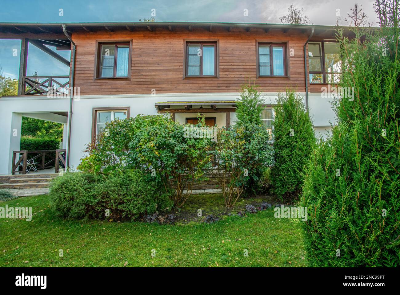 Büsche und grünes Gras und eine Hütte im Chalet-Stil. 2-stöckiges Haus (Hütte) - Sonnentag im Herbst Stockfoto