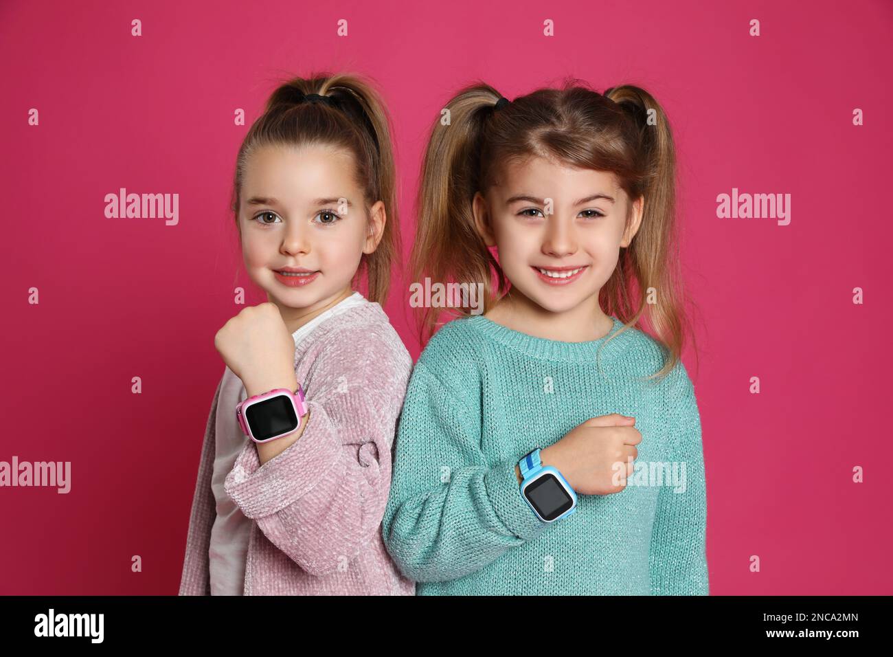 Kleine Mädchen mit Smartwatches auf pinkfarbenem Hintergrund Stockfoto