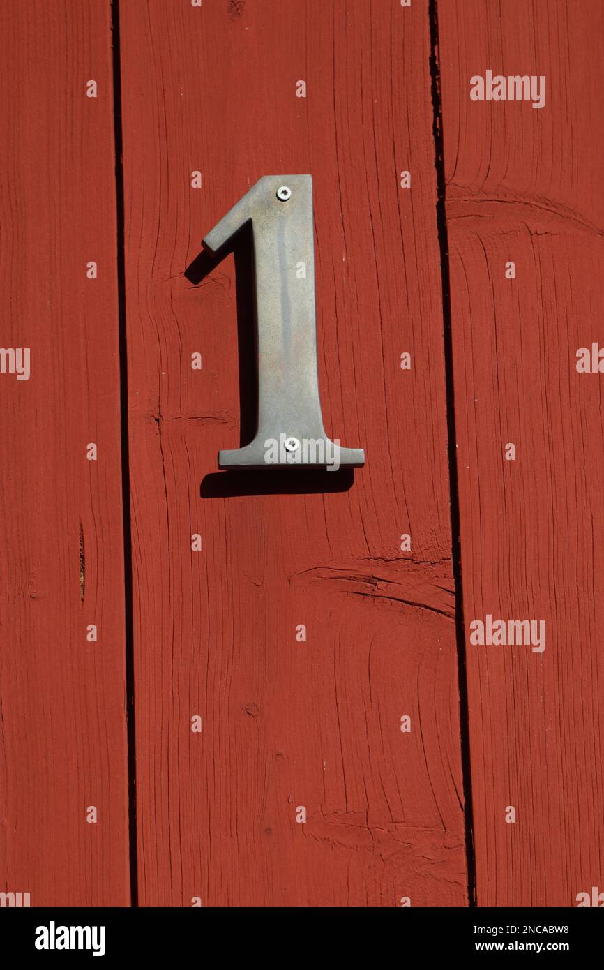 Weißes Schild Nummer eins auf einer roten Tür mit horizontalen Streifen, Hausnummer Stockfoto