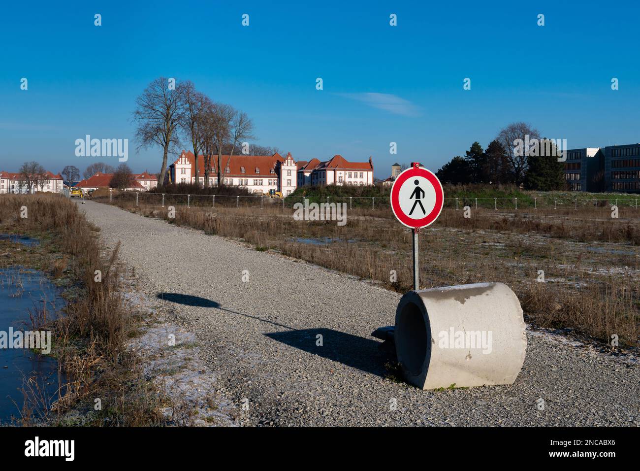 Ein Verbotsschild für Fußgänger und ein Betonring auf einem einsamen Weg, der zu einer Baustelle führt. Im Hintergrund befindet sich ein Gebäude unter einem blauen s. Stockfoto