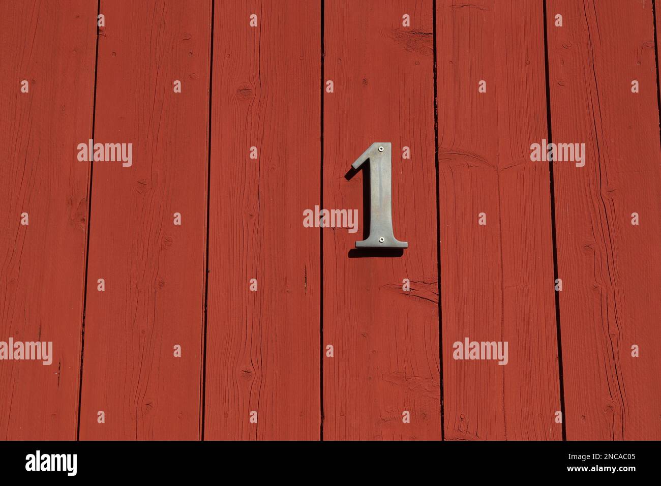 Weißes Schild Nummer eins auf einer roten Tür mit horizontalen Streifen, Hausnummer Stockfoto