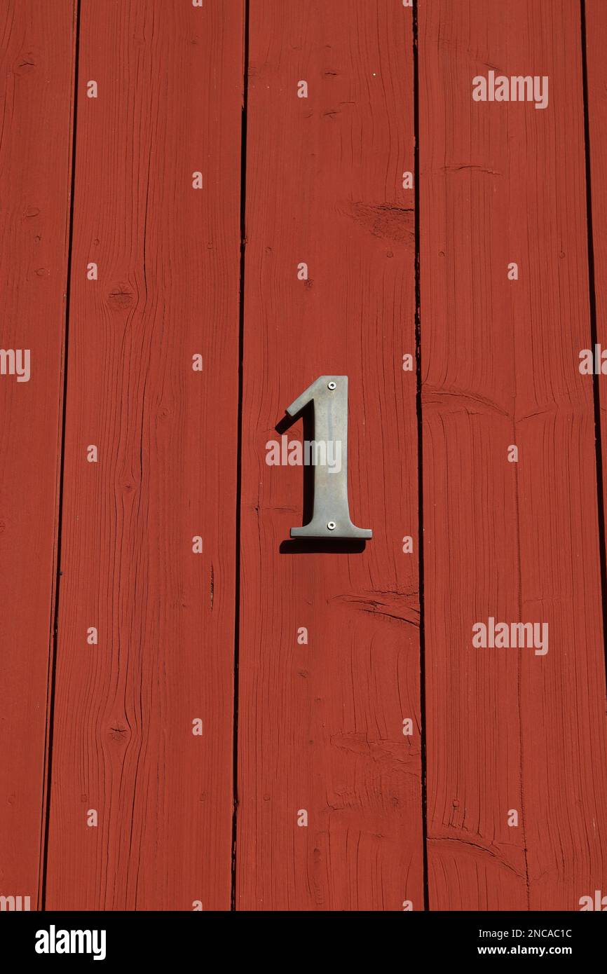 Weißes Schild Nummer eins auf einer roten Tür mit horizontalen Streifen, Hausnummer Stockfoto