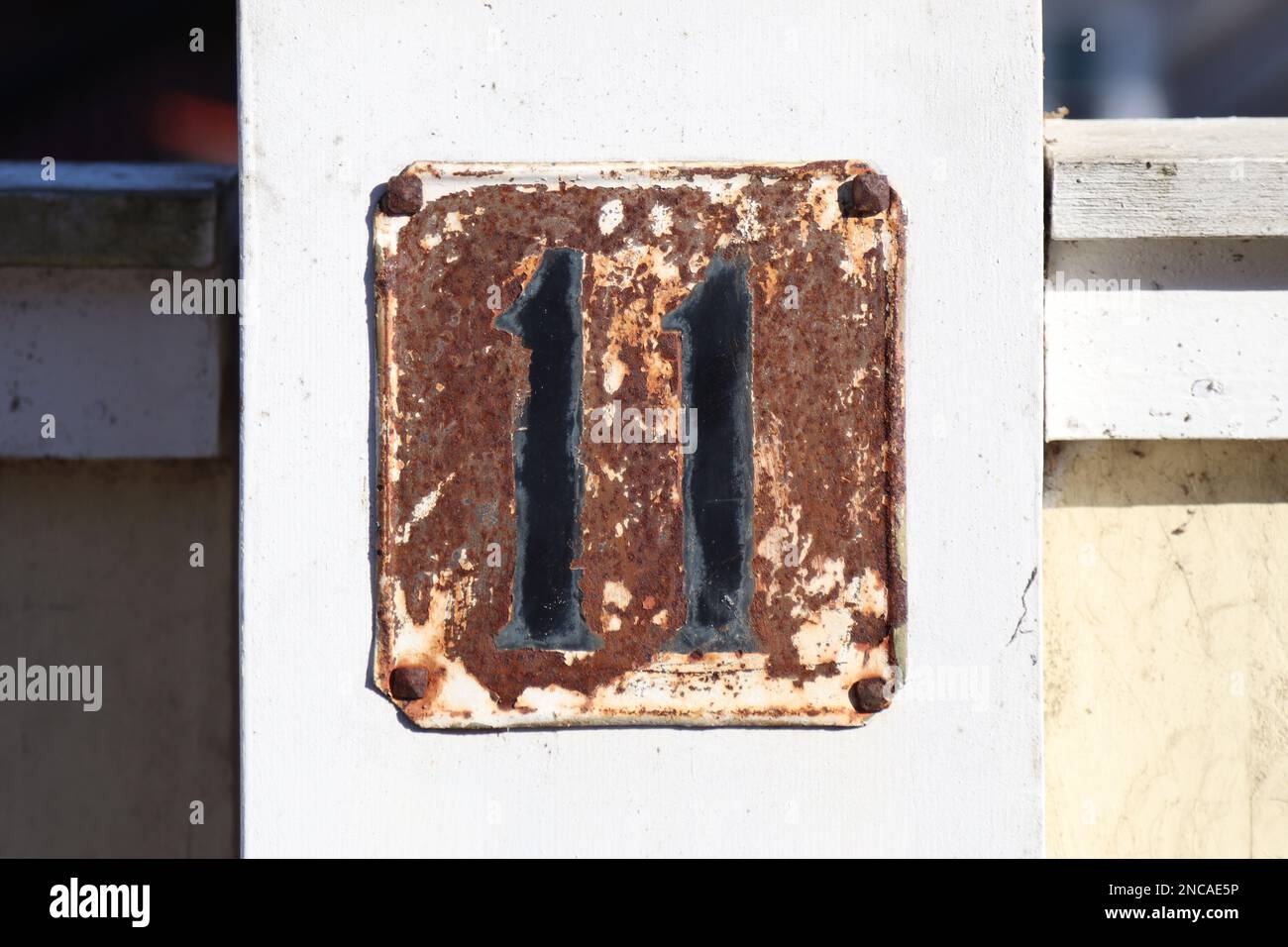 Hausnummer 11 metallisches Adresszeichen, alter rustikaler weißer Hintergrund, schwarze Nummer, 11-stellig Stockfoto