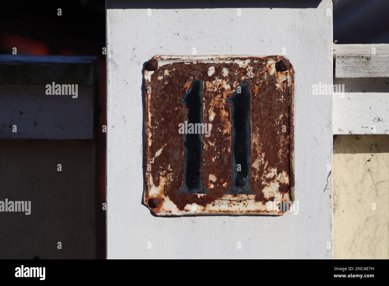 Hausnummer 11 metallisches Adresszeichen, alter rustikaler weißer Hintergrund, schwarze Nummer, 11-stellig Stockfoto