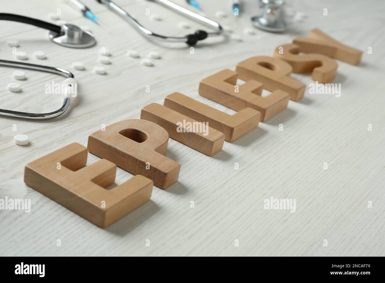 Word Epilepsie aus Holzbuchstaben, Stethoskopen, Pillen und Spritzen auf weißem Tisch, Nahaufnahme Stockfoto
