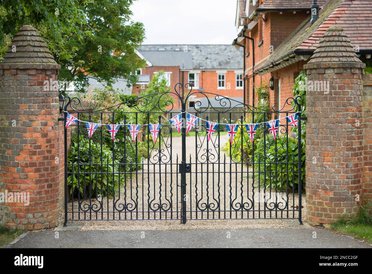 Viktorianisches englisches Landhaus mit Auffahrt und schwarzeisernen Toren, dekoriert mit Union Jack Bunting. Buckinghamshire, England, Großbritannien Stockfoto