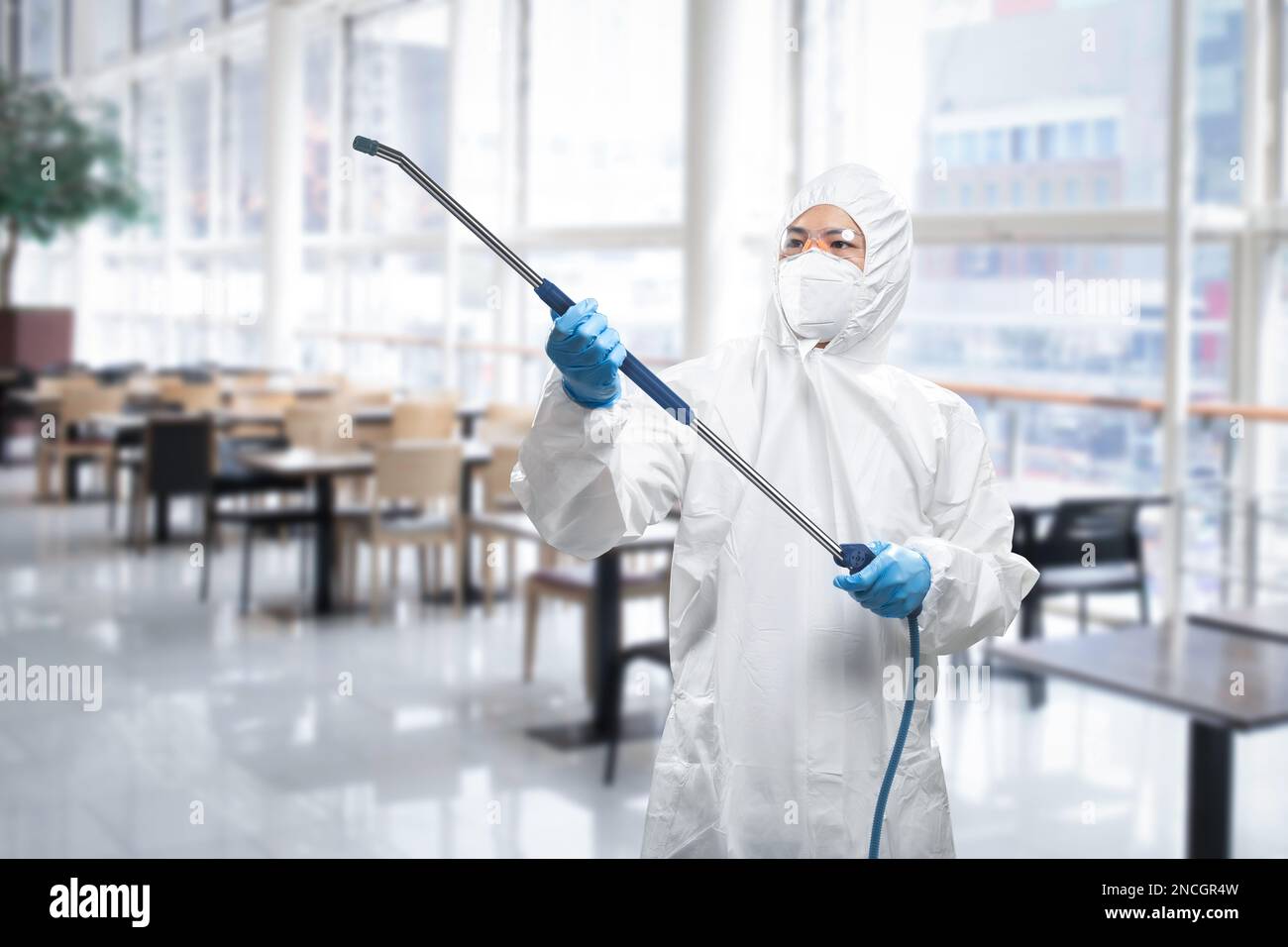 Arbeiter trägt medizinischen Schutzanzug oder weißen Overall Anzug desinfizieren mit Spray im Restaurant Stockfoto