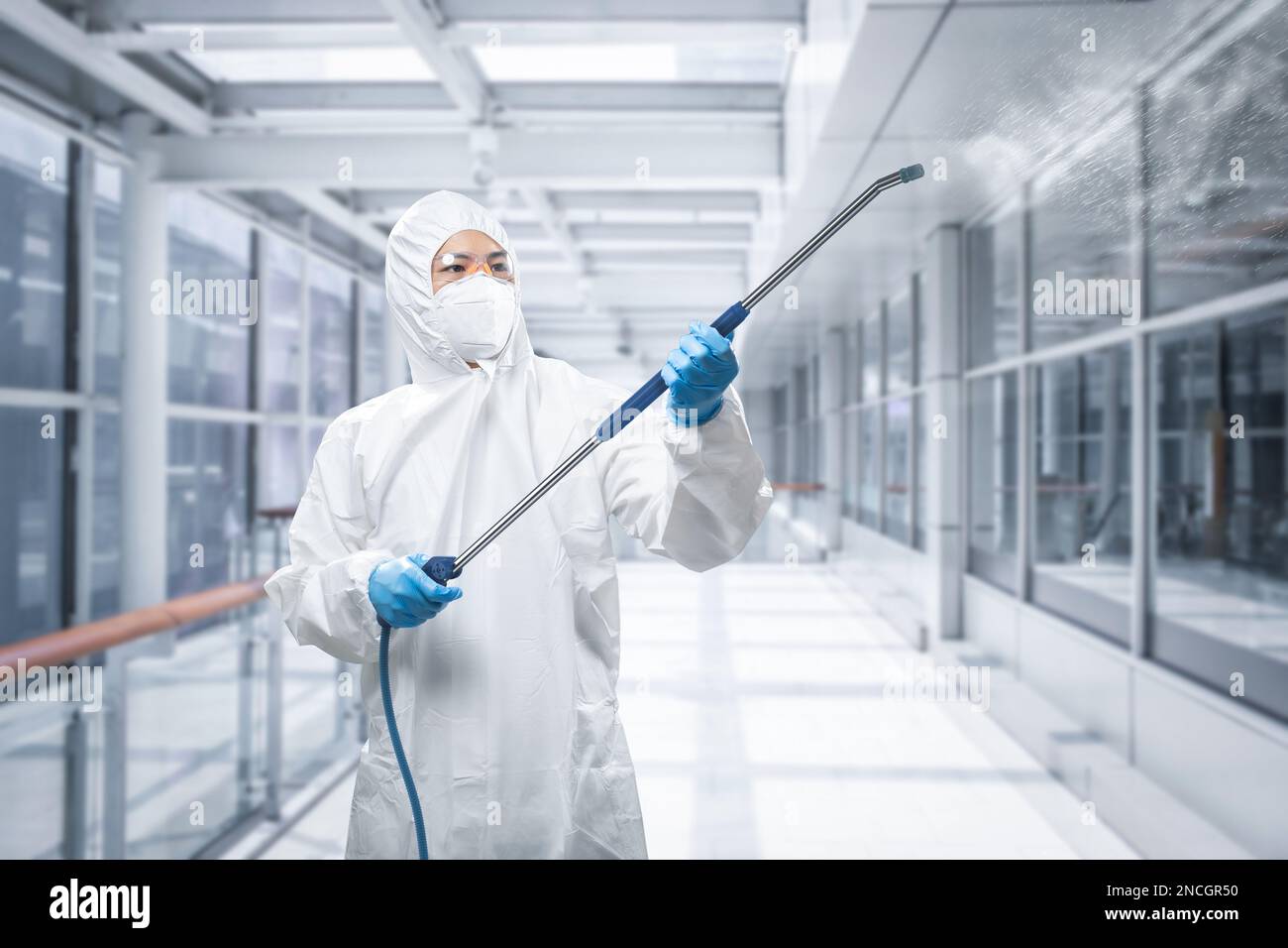 Arbeiter trägt medizinischen Schutzanzug oder weißen Overall Anzug desinfizieren mit Spray im Flur Stockfoto
