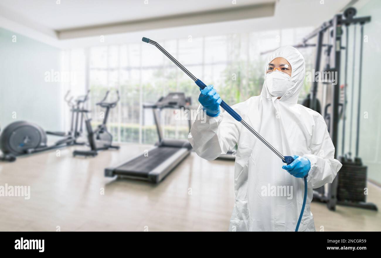 Arbeiter trägt medizinischen Schutzanzug oder weißen Overall Anzug desinfizieren mit Spray im Fitnessstudio Stockfoto