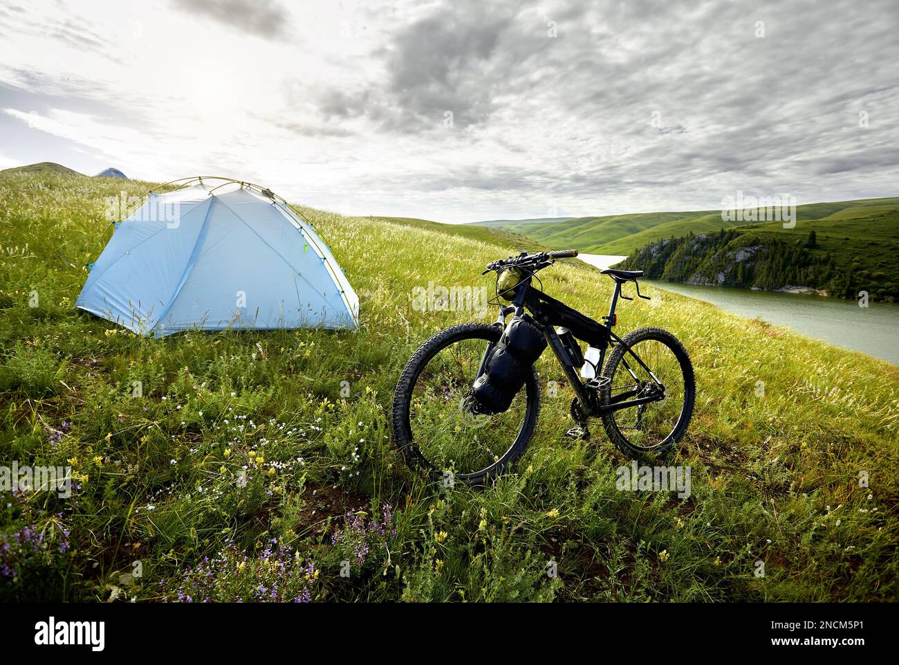 Mountainbike mit Touristentaschen in der Nähe des blauen Zelts Camping auf dem grünen Hügel in der Nähe des Sees im Bergtal in Kasachstan. Extreme Sport-Fahrradfahren und Stockfoto
