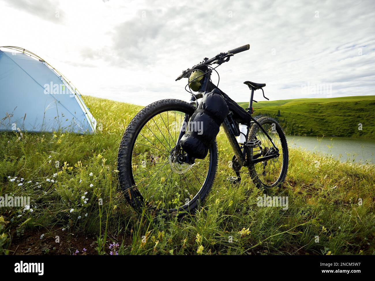 Mountainbike mit Touristentaschen in der Nähe des blauen Zelts Camping auf dem grünen Hügel in der Nähe des Sees im Bergtal in Kasachstan. Extreme Sport-Fahrradfahren und Stockfoto