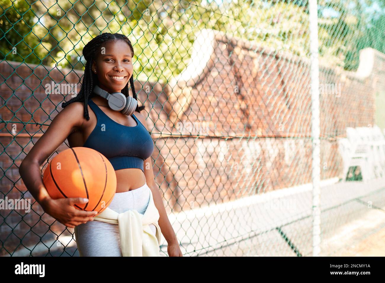 Basketball - das liegt mir im Blut. Porträt einer sportlichen jungen Frau, die im Freien einen Basketball hält und an einem Zaun steht. Stockfoto